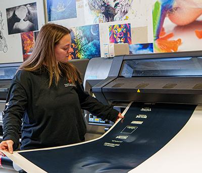 Woman watching a large scale printer produce a custom vending machine graphic